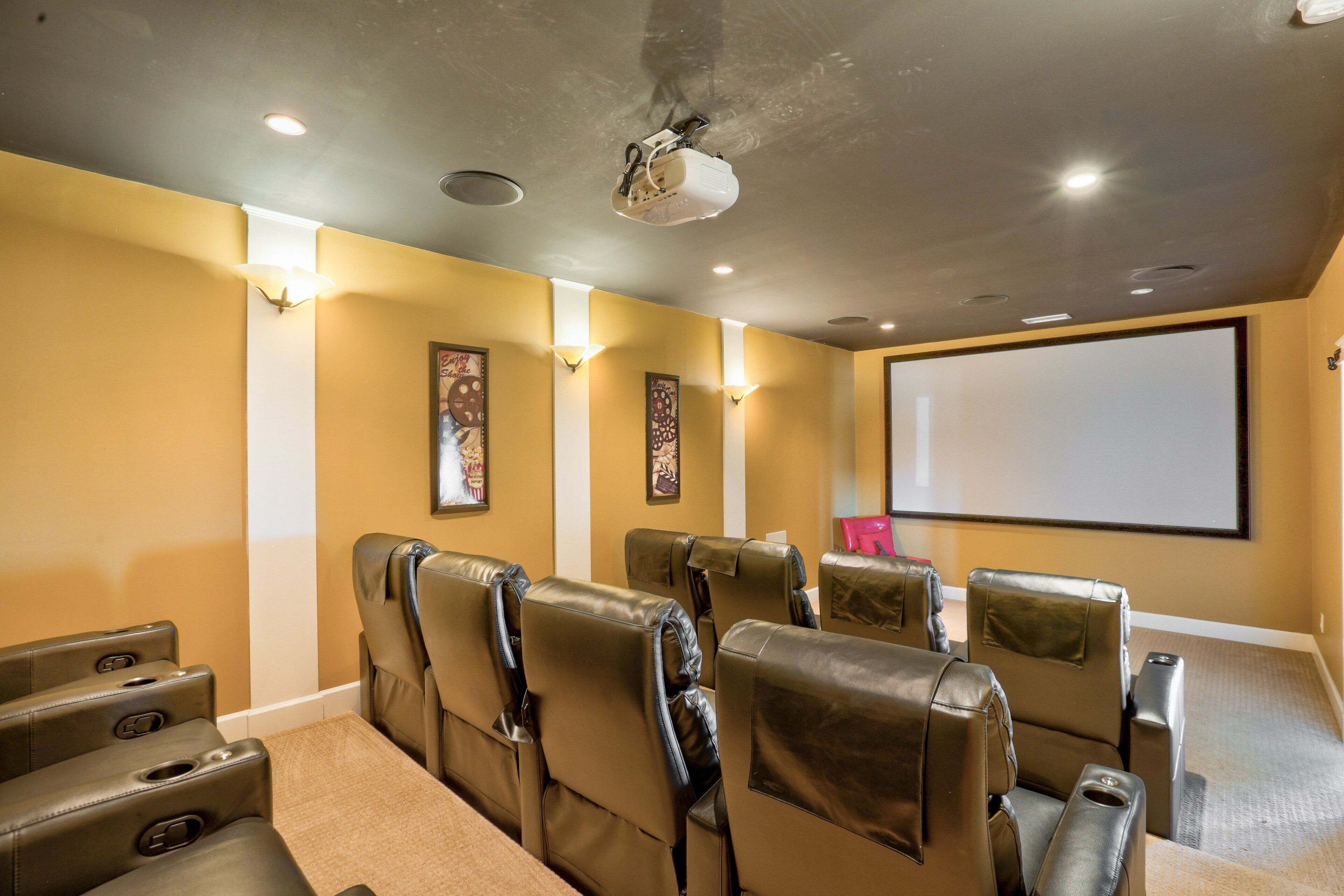 Una sala de cine en casa con sillones de cuero reclinables, una pantalla grande y parlantes instalados en la pared.