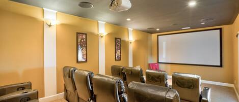 Una sala de cine en casa con sillones de cuero reclinables, una pantalla grande y parlantes instalados en la pared.