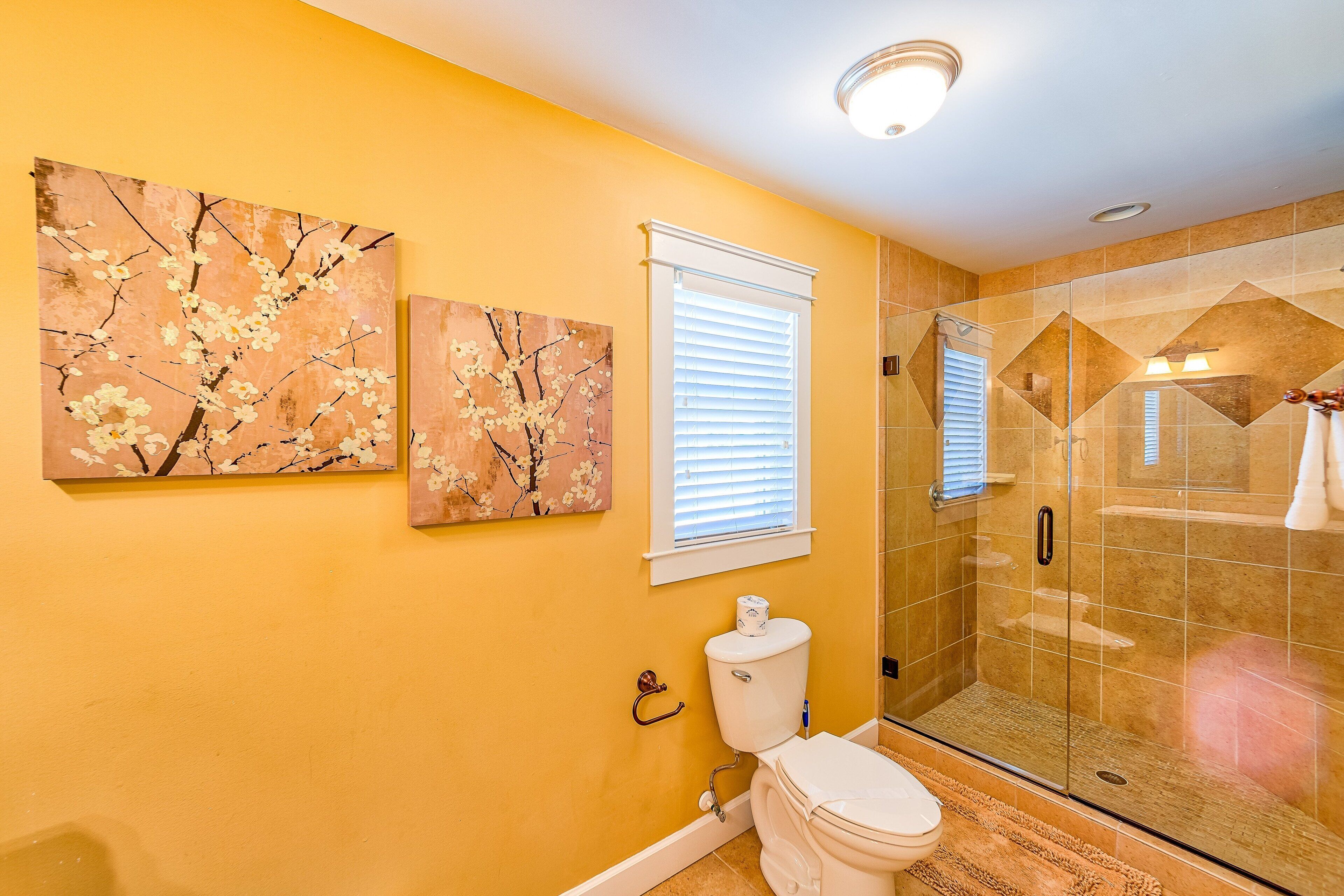 A bathroom with a toilet, a shower with glass doors, and two wall-mounted paintings.
