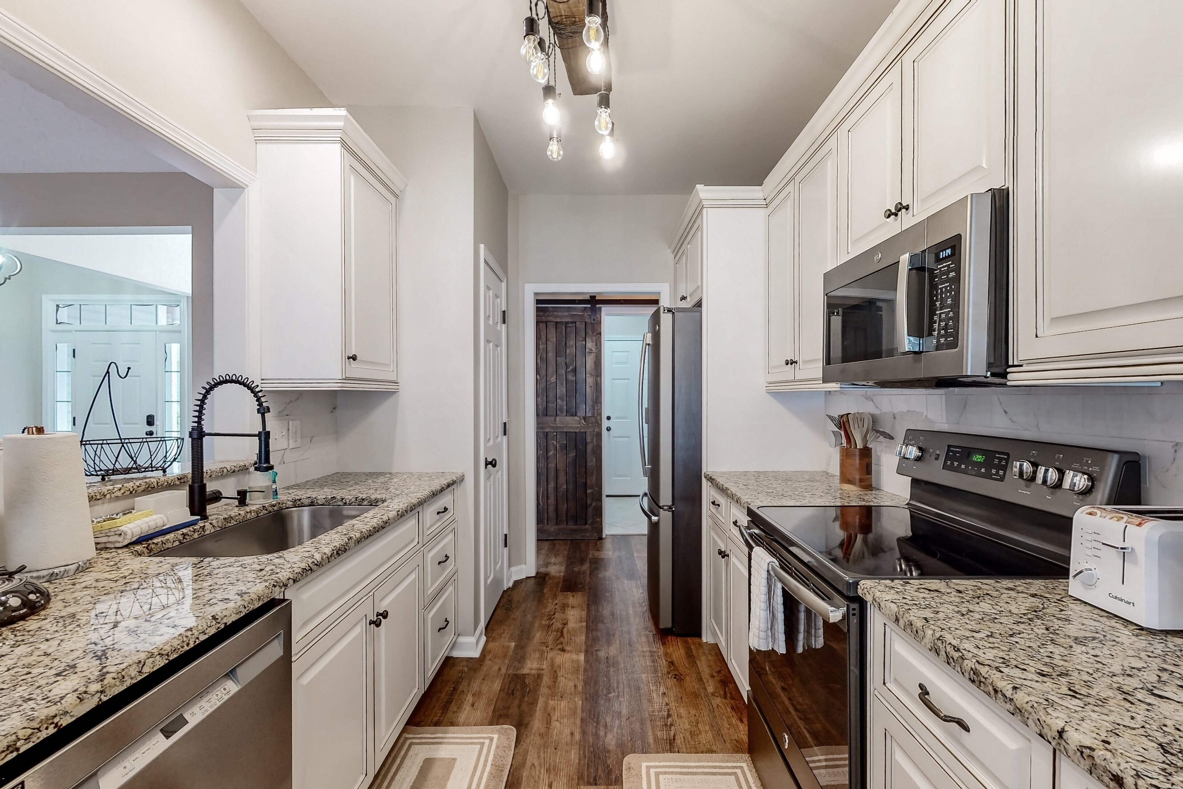 A modern kitchen with white cabinetry, granite countertops, stainless steel appliances, and a wooden floor.