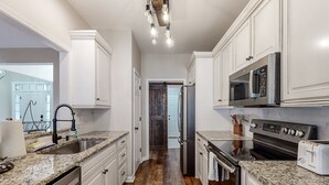 A modern kitchen with white cabinetry, granite countertops, stainless steel appliances, and a wooden floor. - Dog-friendly coastal home with lovely patio, pool, & games - near beaches & golf (Calabash)