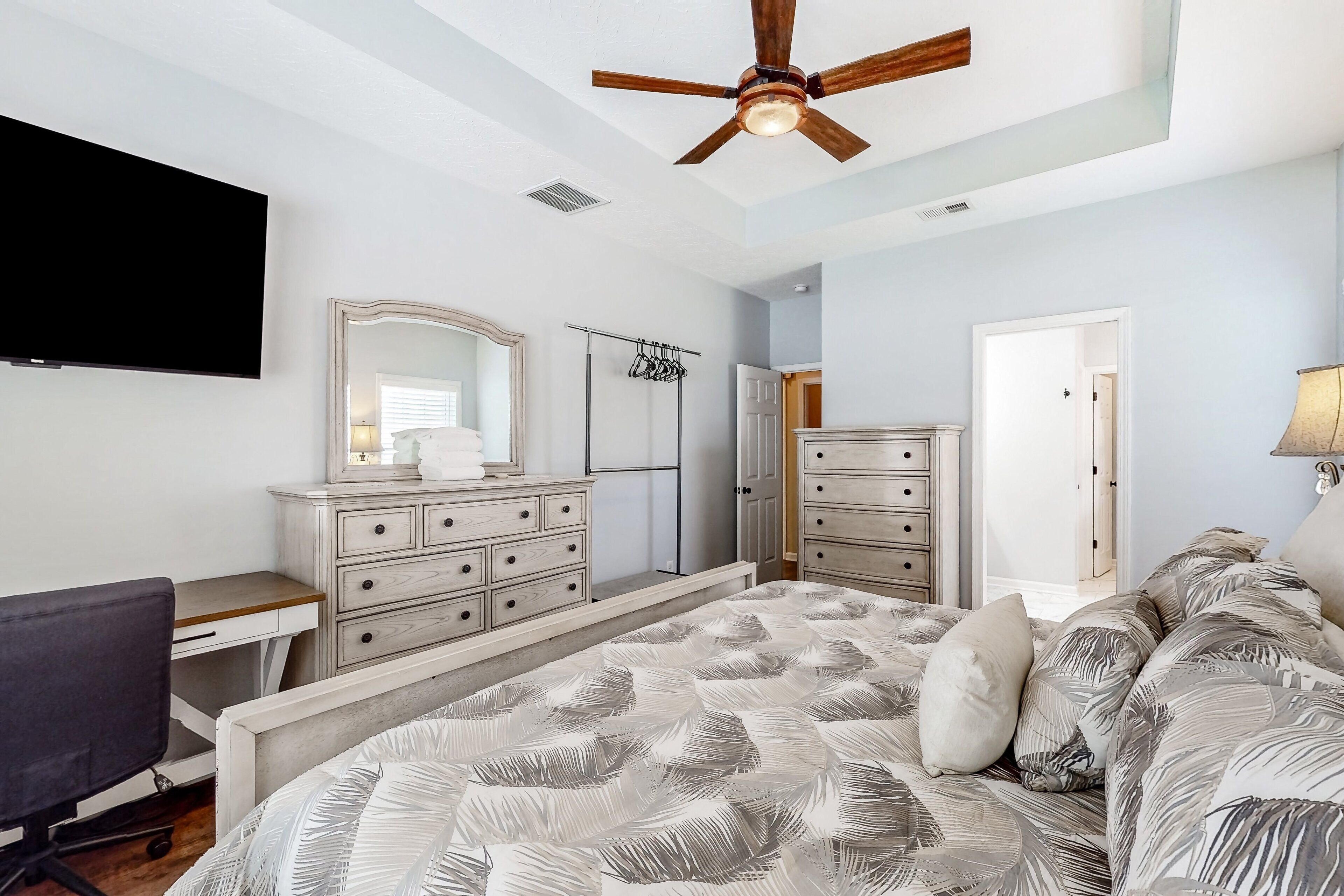 A bedroom with a bed, a desk, a dresser, a mirror, and a ceiling fan.