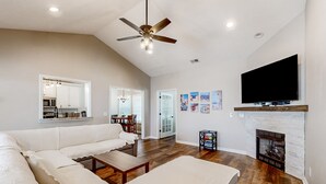 A spacious living room with a large sectional sofa, a fireplace, a mounted TV, and a ceiling fan. - Dog-friendly coastal home with lovely patio, pool, & games - near beaches & golf (Calabash)