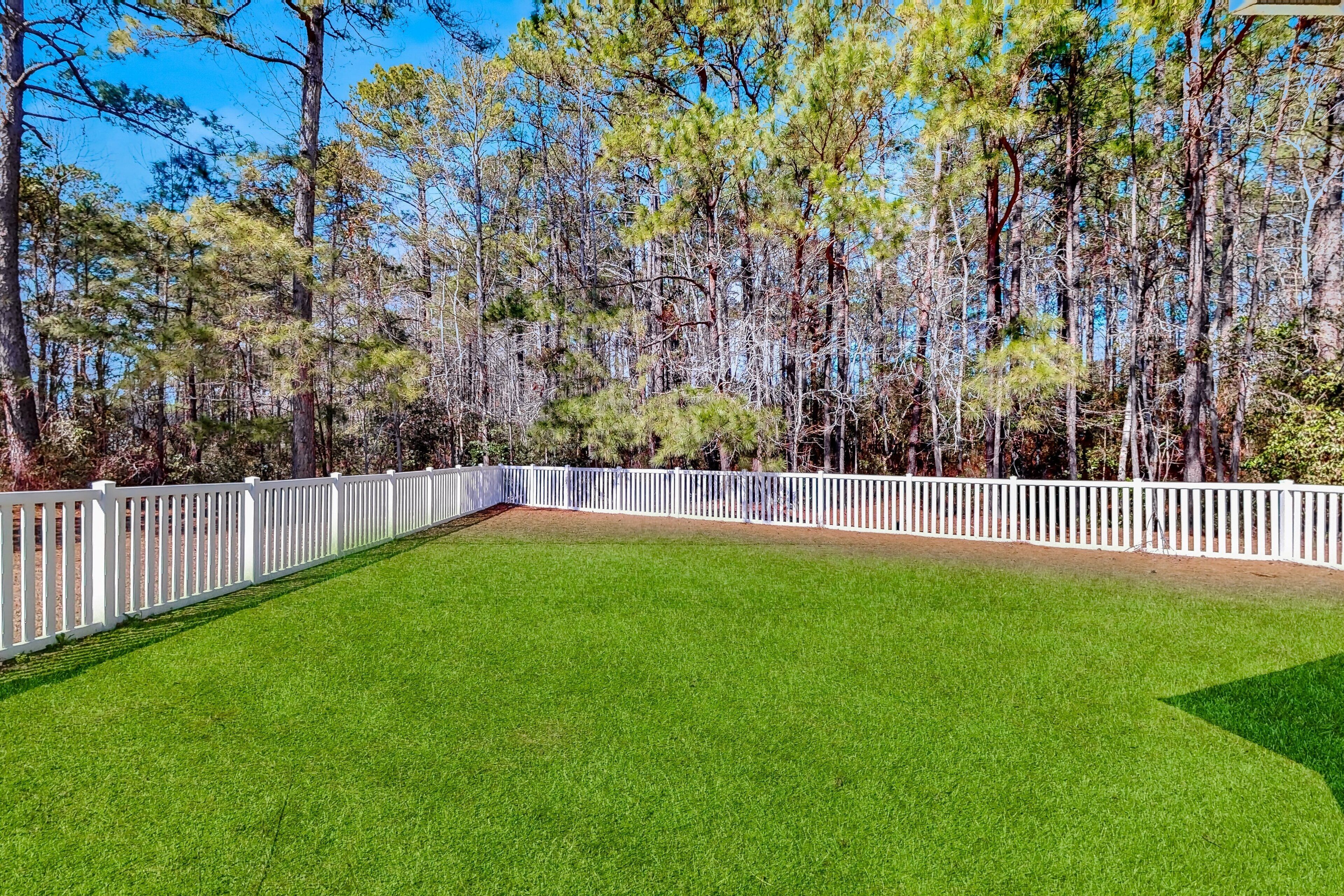 A well-maintained grassy area with a white fence and tall trees in the background.