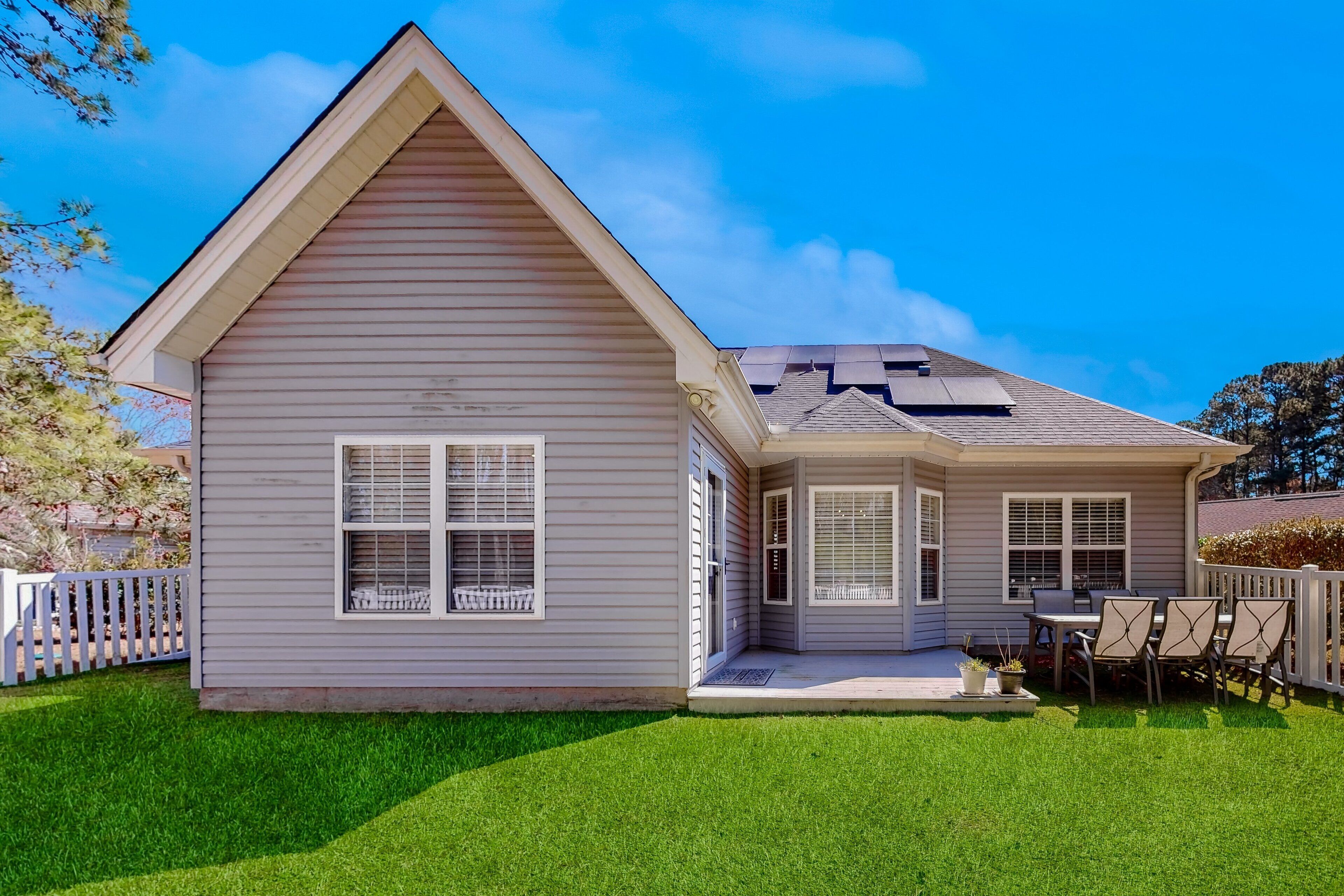 A two-story house with a gabled roof, a covered porch with a table and chairs, and a well-maintained lawn.