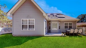 A two-story house with a gabled roof, a covered porch with a table and chairs, and a well-maintained lawn. - Dog-friendly coastal home with lovely patio, pool, & games - near beaches & golf (Calabash)