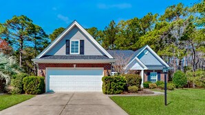 A two-story house with a garage, surrounded by well-maintained lawns and trees. - Dog-friendly coastal home with lovely patio, pool, & games - near beaches & golf (Calabash)