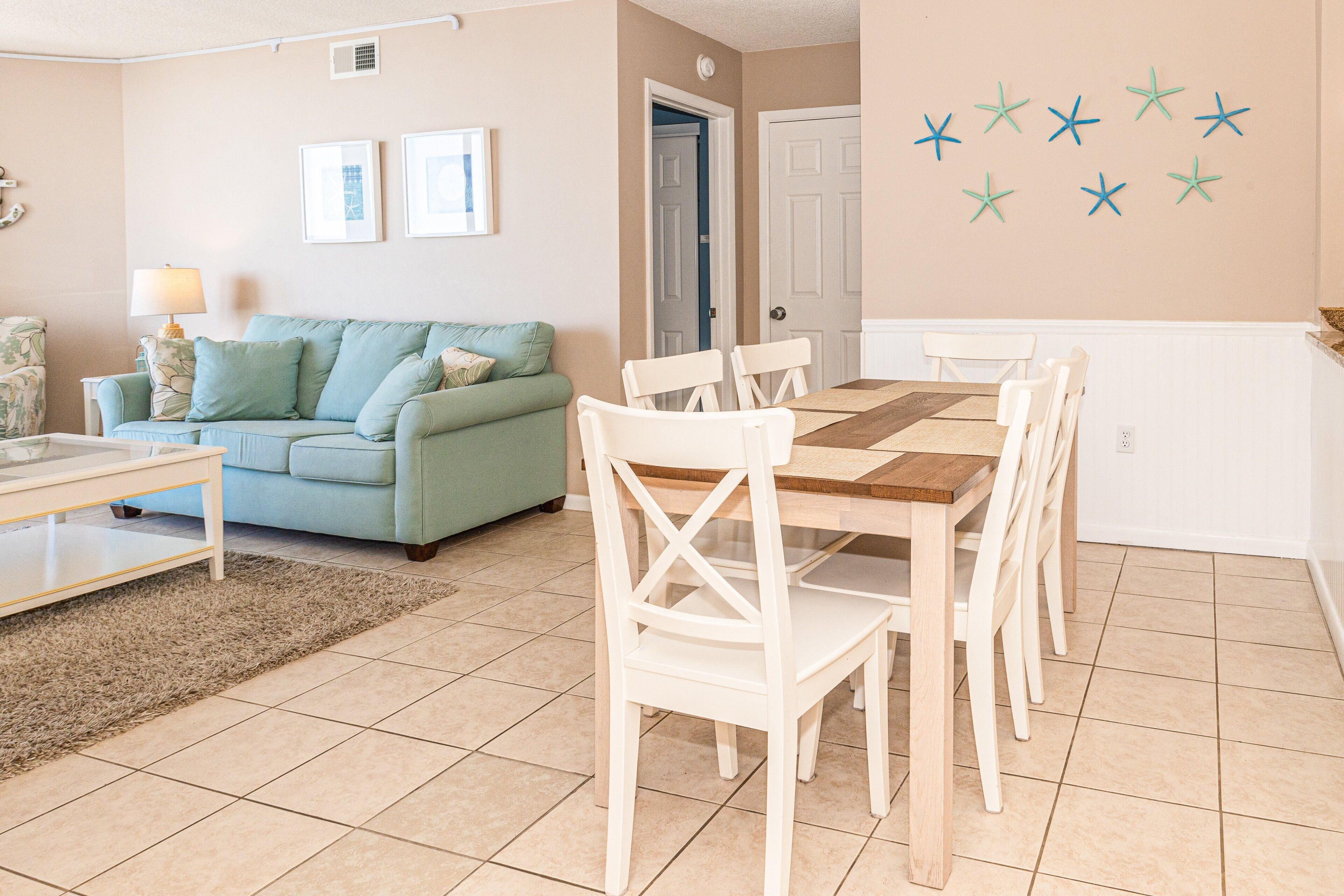 Un salon avec un canapé vert, des chaises blanches, une table à manger en bois et un sol carrelé.