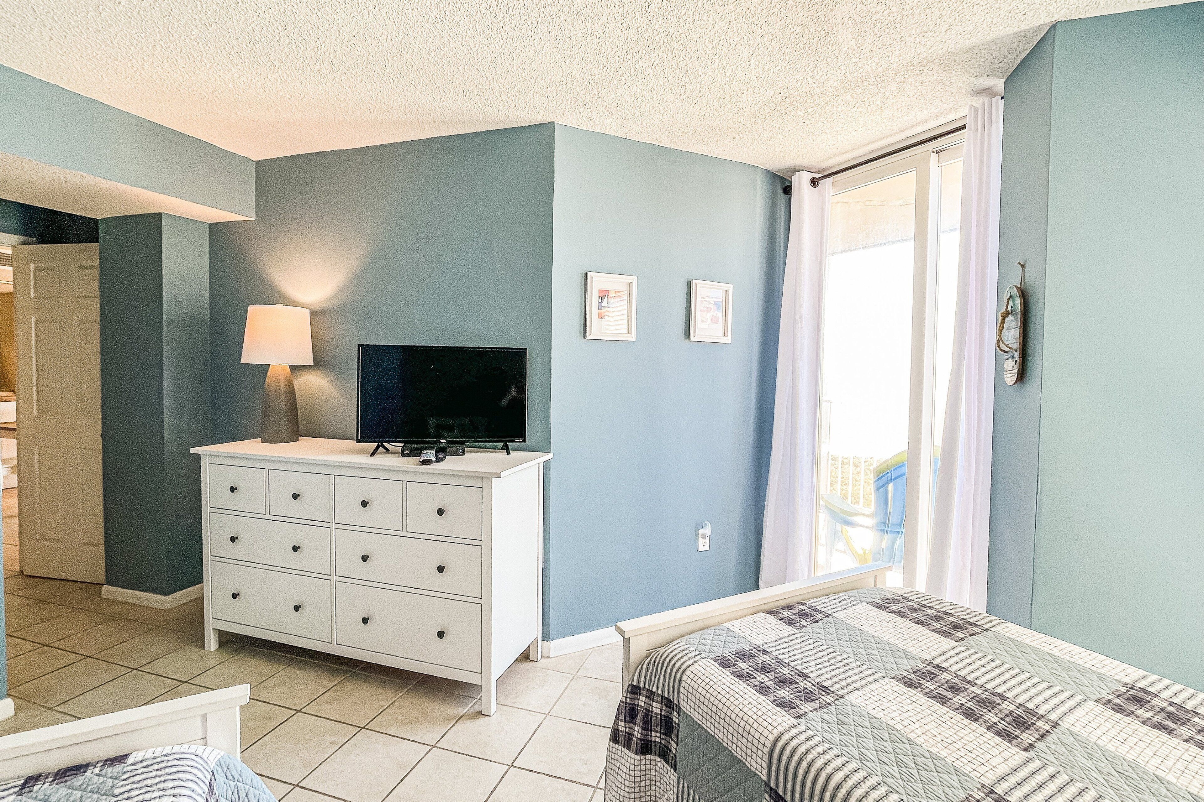 A bedroom with a bed, a dresser, a television, and a window with curtains.