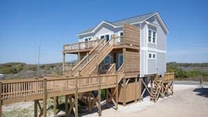 Una casa frente al mar con terraza de madera, varios niveles y una escalera que lleva al piso superior.