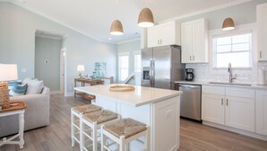 Cocina moderna con armarios blancos, una isla central con taburetes, un refrigerador de acero inoxidable y una cafetera.