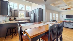 A modern kitchen with dark cabinets, a wooden dining table, and a ceiling fan. - Slowin' Dune | Lavish Island Getaway with Golf Cart Near Beach, Golf, & Dining (Caswell Beach)