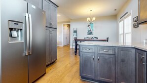 A modern kitchen with stainless steel appliances, dark cabinetry, and a wooden floor. - Slowin' Dune | Lavish Island Getaway with Golf Cart Near Beach, Golf, & Dining (Caswell Beach)