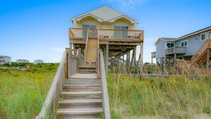 Ein Strandhaus mit einer Holztreppe, die zu einem Balkon führt.
