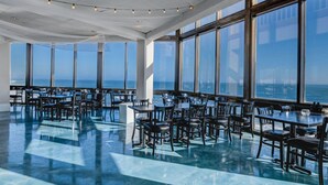 A spacious dining area with large windows and a view of the ocean. Tables and chairs are arranged for dining. - 2nd-floor beachfront condo with ocean views, pool, sauna, tennis, balcony, & AC (North Topsail Beach)