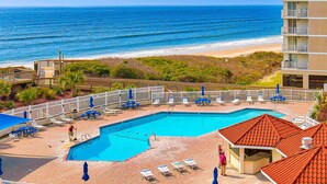 A pool area with a view of the ocean, surrounded by lounge chairs and umbrellas. - 2nd-floor beachfront condo with ocean views, pool, sauna, tennis, balcony, & AC (North Topsail Beach)