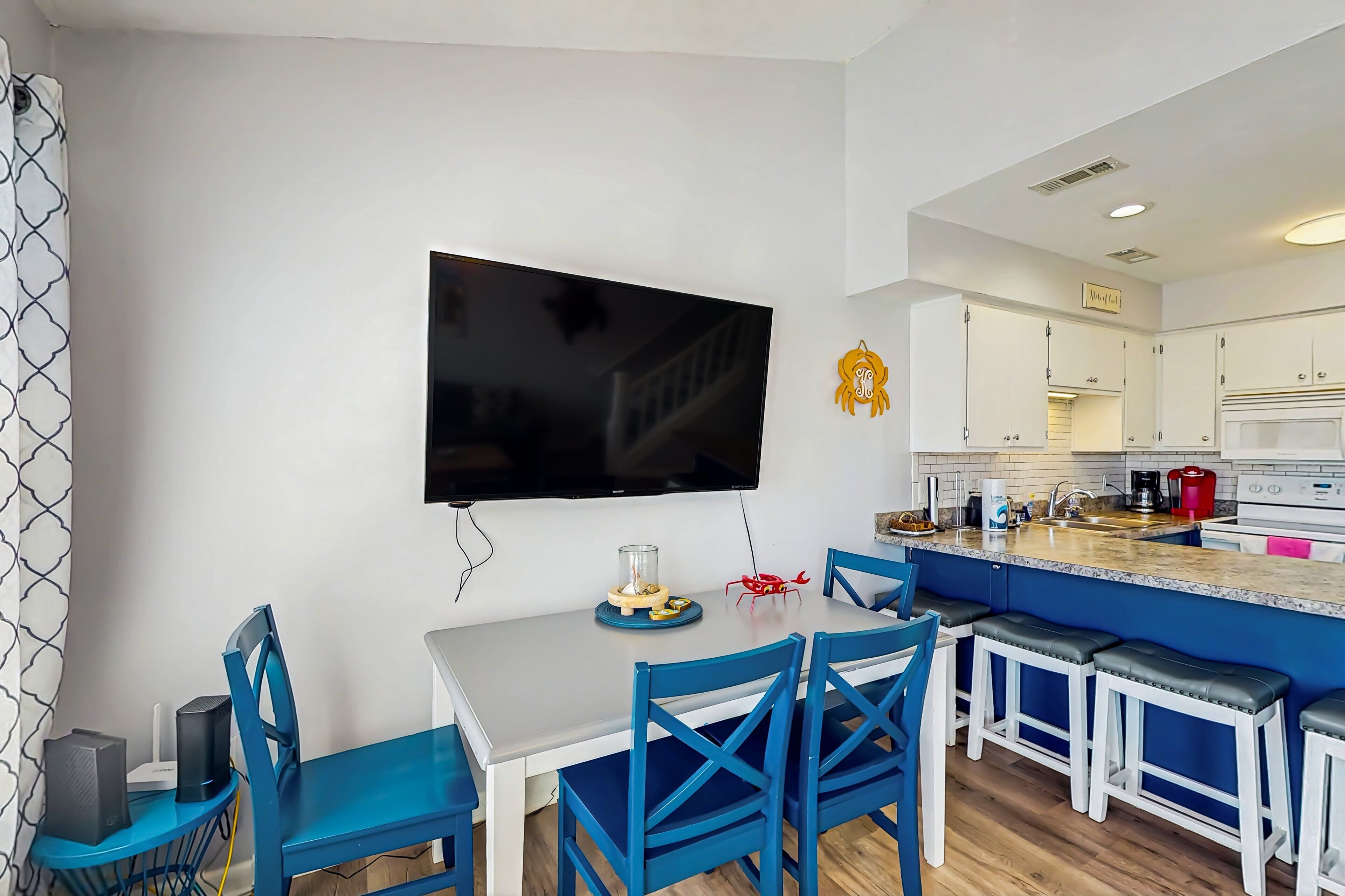 A modern kitchen with white cabinets, a blue island, and a flat-screen TV mounted on the wall.