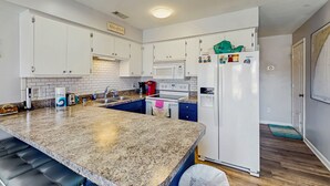 Une cuisine avec des meubles blancs, un plan de travail en granit, un four encastré et un réfrigérateur décoré d’aimants.