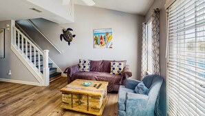 Un salon avec un escalier, un canapé violet, un fauteuil bleu et une commode en bois.