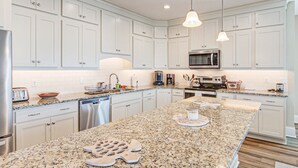 Una cocina moderna con armarios blancos, encimeras de granito, electrodomésticos de acero inoxidable e iluminación colgante.