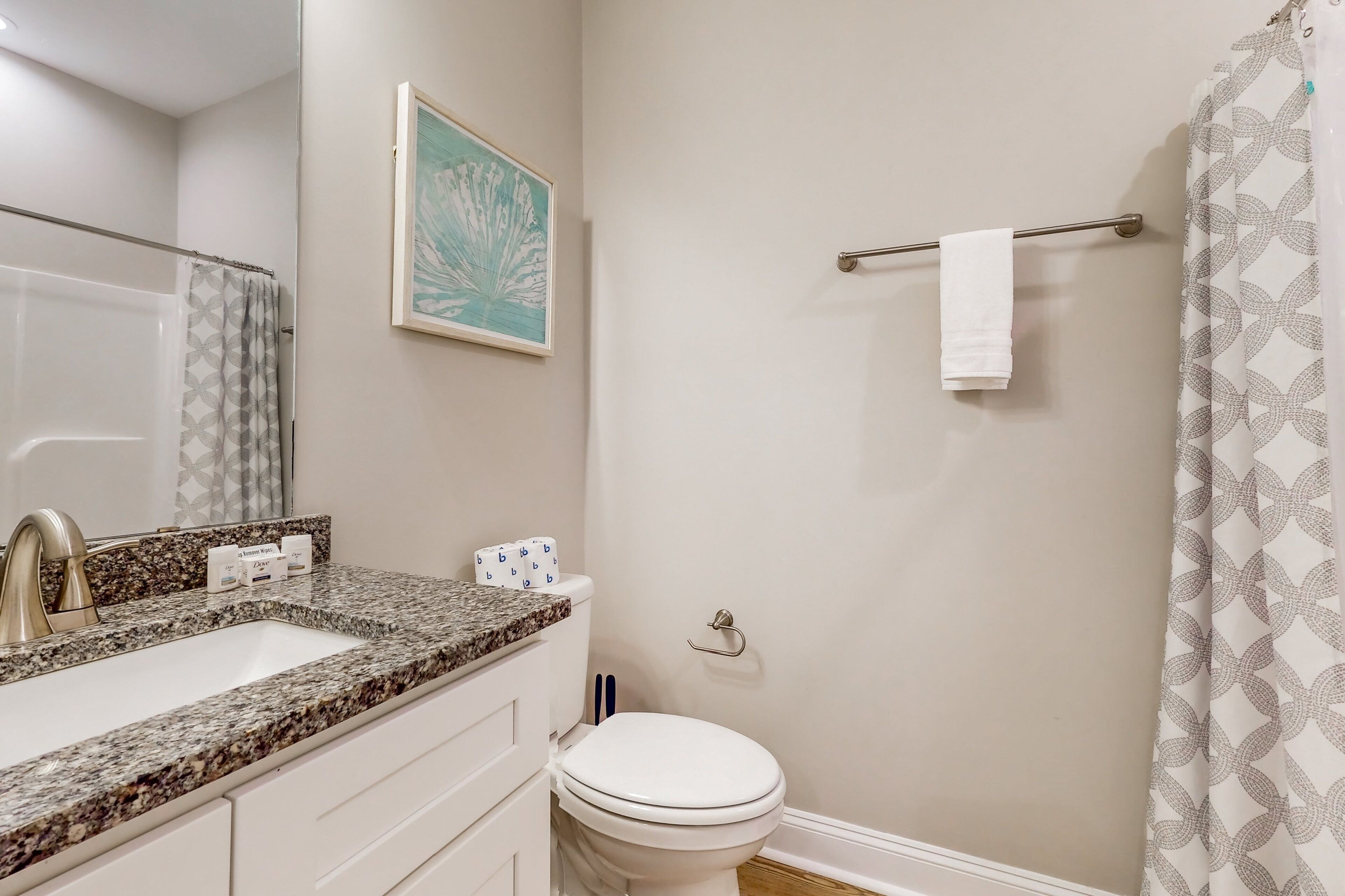 A bathroom with a granite countertop sink, a white toilet, a shower curtain with a geometric pattern, and a towel rack with a white towel.