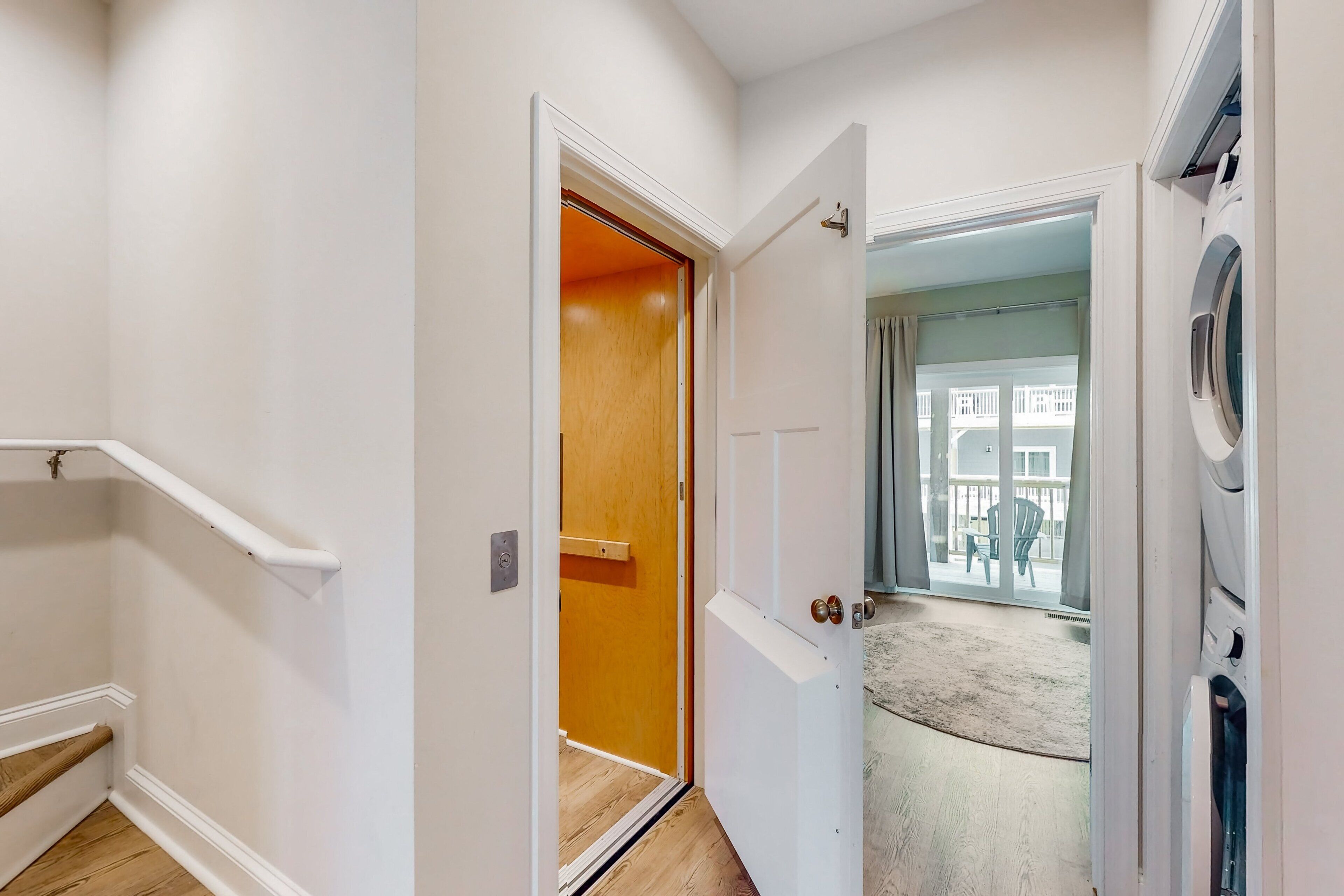 A hallway with a wooden door leading to a balcony with a view of buildings.