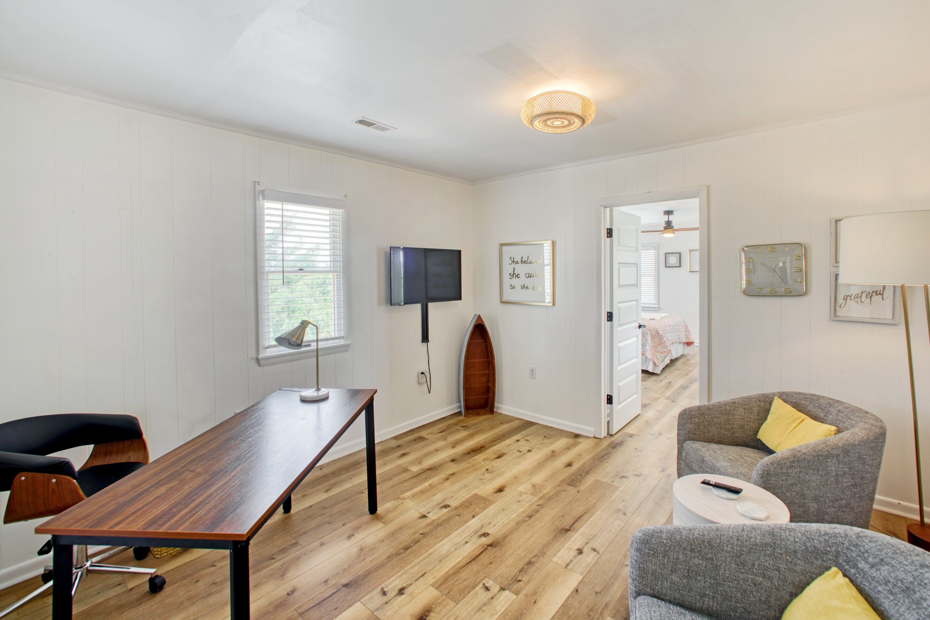 A room with a wooden floor, a desk, a chair, a television, and a door leading to another room.
