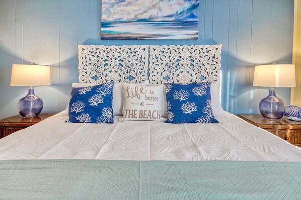 A bed with a white bedspread, two decorative pillows with blue and white patterns, a white headboard with intricate designs, and two bedside lamps on wooden nightstands.