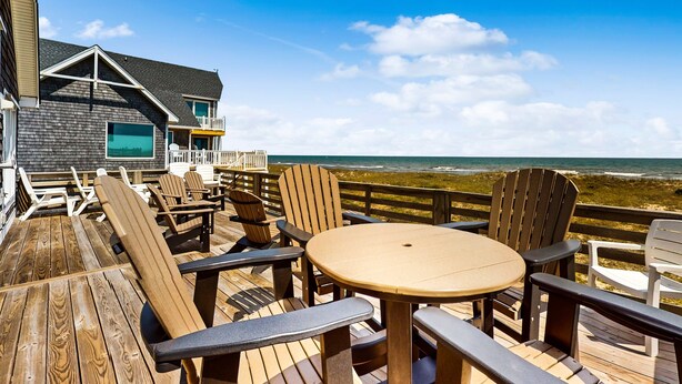 Une terrasse en bois, agréée de mobilier d’extérieur, donnant sur une plage.