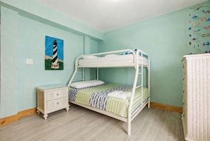 A bunk bed with a white frame, a bedside table with drawers, and a wall with a painting. - Three-story beachfront home with private pool, hot tub, decks, & ocean views (Hatteras)