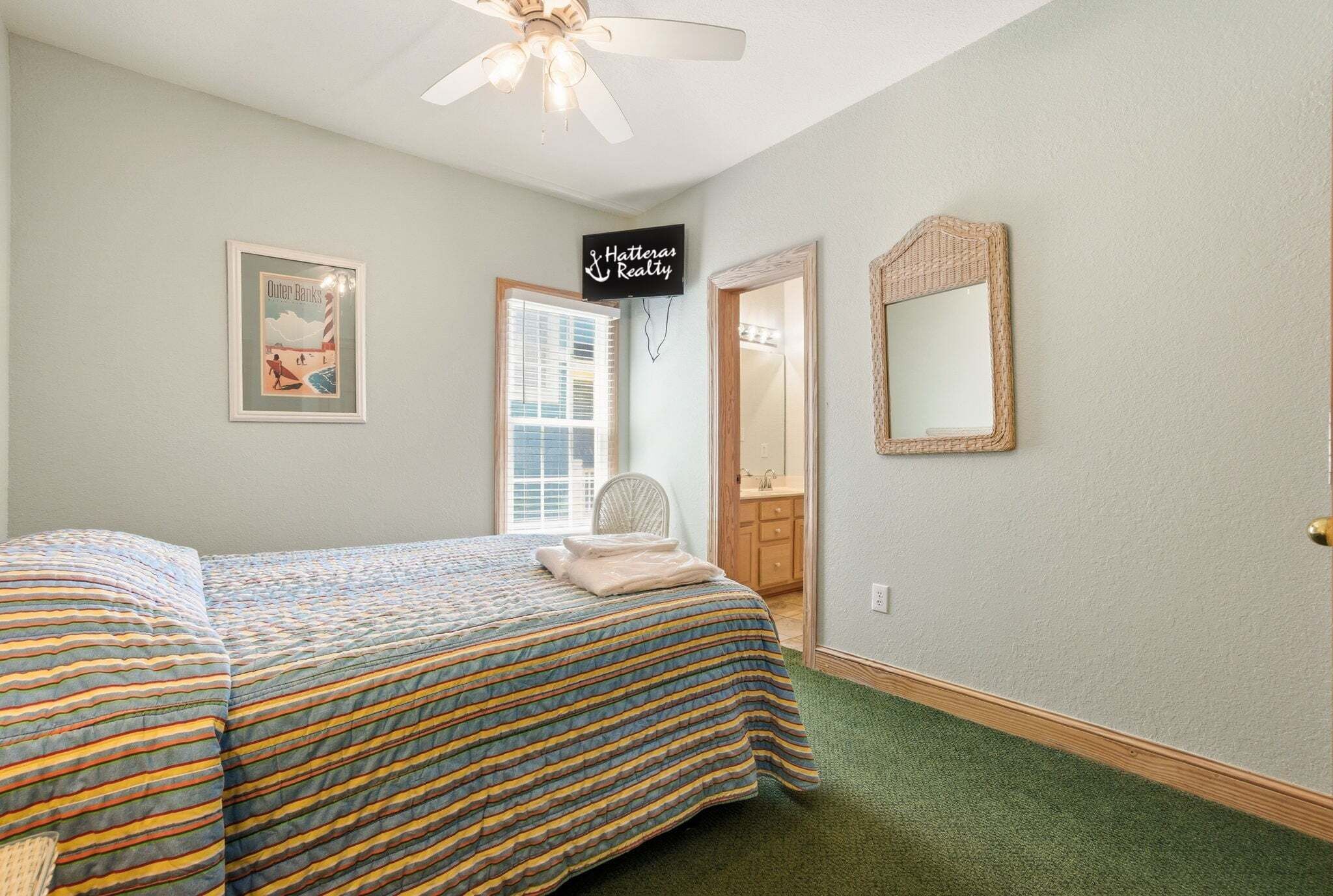 A bedroom with a bed, a ceiling fan, a framed picture, a mirror, and a sign on the wall.
