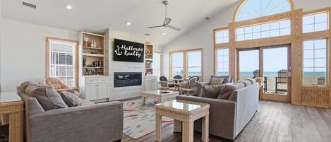 A spacious living room with a fireplace, large windows, and a view of the ocean.