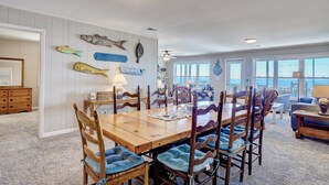 Un coin repas avec une table et des chaises en bois, un mur décoré de motifs de poissons et une enseigne indiquant « MAISON DE PLAGE ».