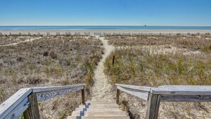 Un escalier en bois mène à une plage d’où l’on a une vue dégagée sur l’océan.