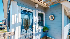 Una casa con fachada azul, una puerta de vidrio con un marco metálico decorativo, una corona en la pared y una planta en maceta en el porche.