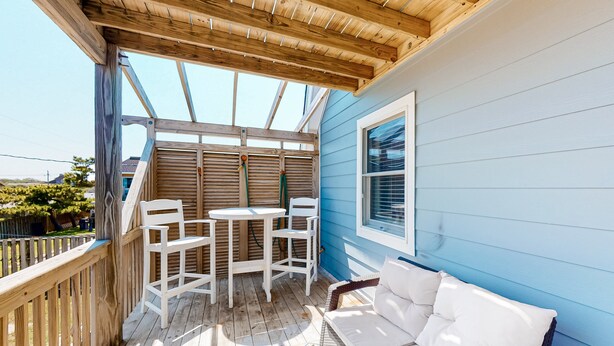 Un patio techado al aire libre con piso de madera, mobiliario blanco y pared azul.