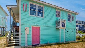 A turquoise two-story house with a pink door, numbered 1049, and a visible staircase leading to the entrance.
