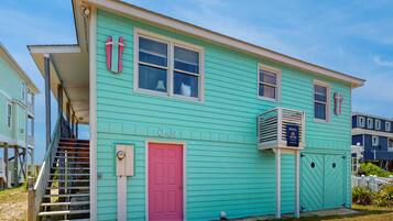 A turquoise two-story house with a pink door, numbered 1049, and a visible staircase leading to the entrance.