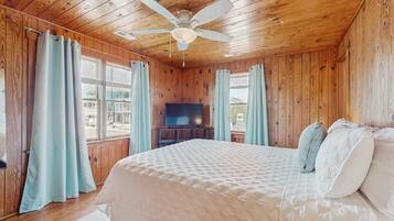 A wooden-paneled bedroom with a bed, curtains, a ceiling fan, and a TV.