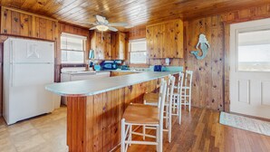 A wooden cabin kitchen with a central island, bar stools, a refrigerator, and a microwave.
