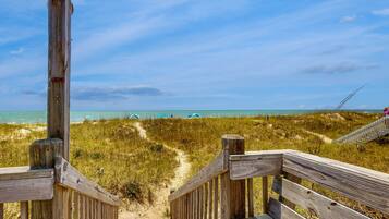 A wooden boardwalk leading to a beach with dunes and a clear sky.