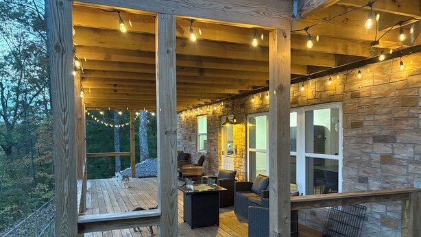 Een houten terras met buitenmeubilair, stenen muren en lichtslingers.