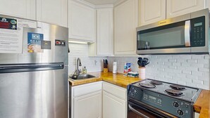 Una cocina moderna con armarios blancos, un refrigerador de acero inoxidable, un microondas y una estufa a gas.