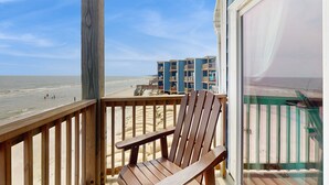 Una terraza de madera con una silla de madera, con vista a una playa y un edificio al fondo.