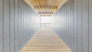 Un pasillo largo y estrecho con suelo de madera y paredes grises, que conduce a un balcón.