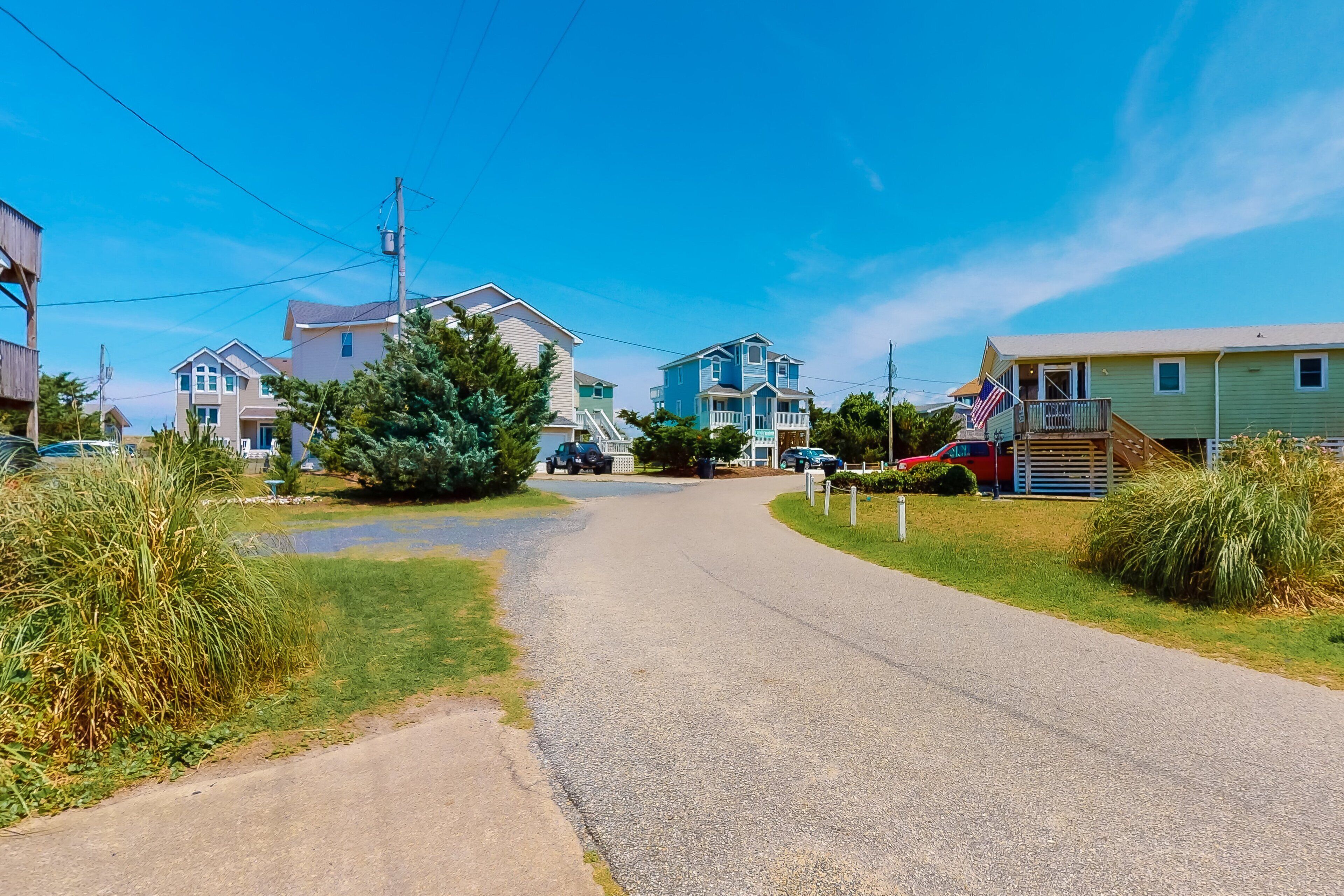 Une rue résidentielle bordée de maisons, avec un ciel dégagé et un petit plan d’eau.