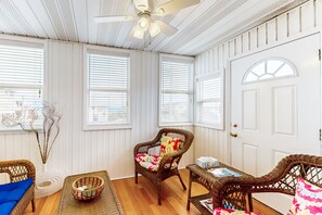 Ein Zimmer mit Deckenventilator, Korbmöbeln und weißen Wandverkleidungen.