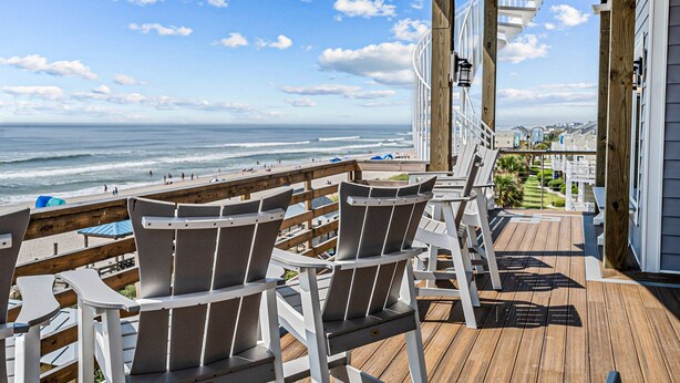 Une terrasse en bois avec des fauteuils Adirondack donnant sur une plage.