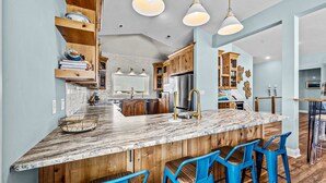 Une cuisine moderne avec un îlot en marbre, des armoires en bois et des tabourets de bar bleus.