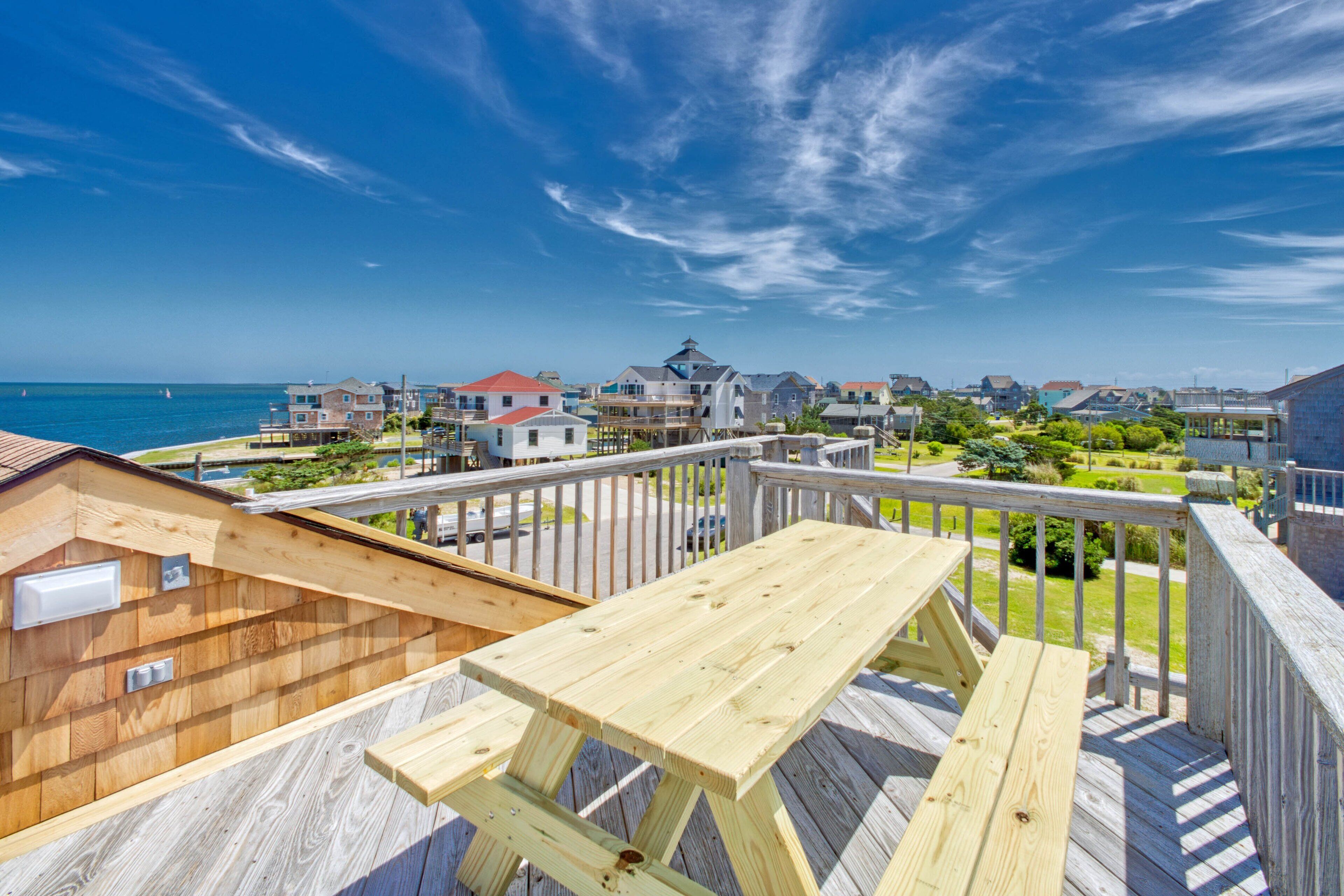 A wooden deck with a picnic table overlooking a coastal town with houses and a clear blue sky.